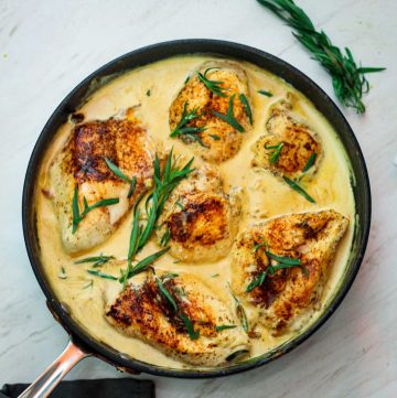A skillet with a creamy chicken dish shown garnished with tarragon leaves.