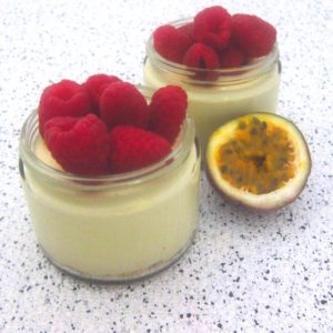 Two jars with passion fruit mousse topped with raspberries shown next to an actual passion fruit cut in half.