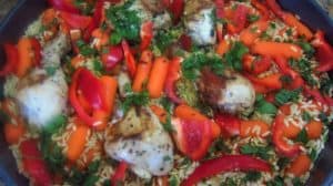 Prepping baking tray with chicken, orzo and veggies