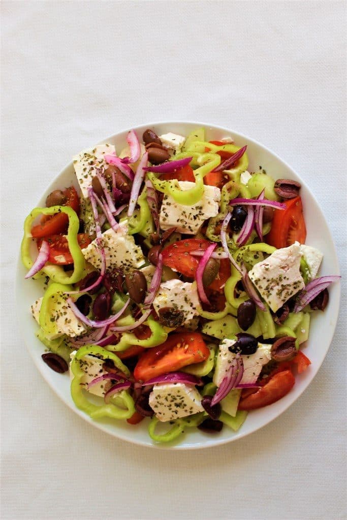 Greek Salad served in a round dish. It's made with tomatoes, cucumbers, feta cheese, red onion, olives etc.