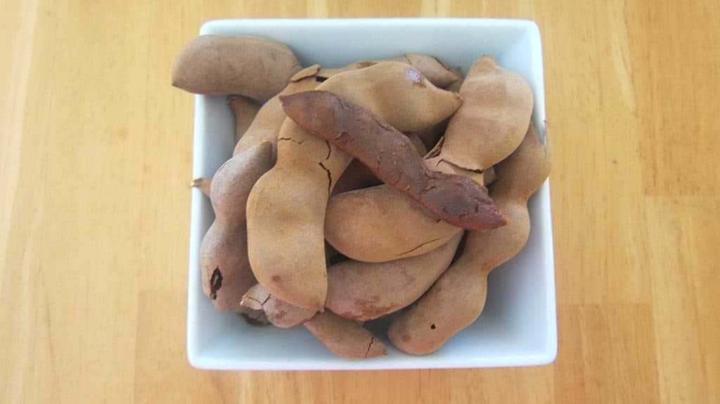 A bowl full of tamarind fruits. I peeled one so you can see how it looks inside.