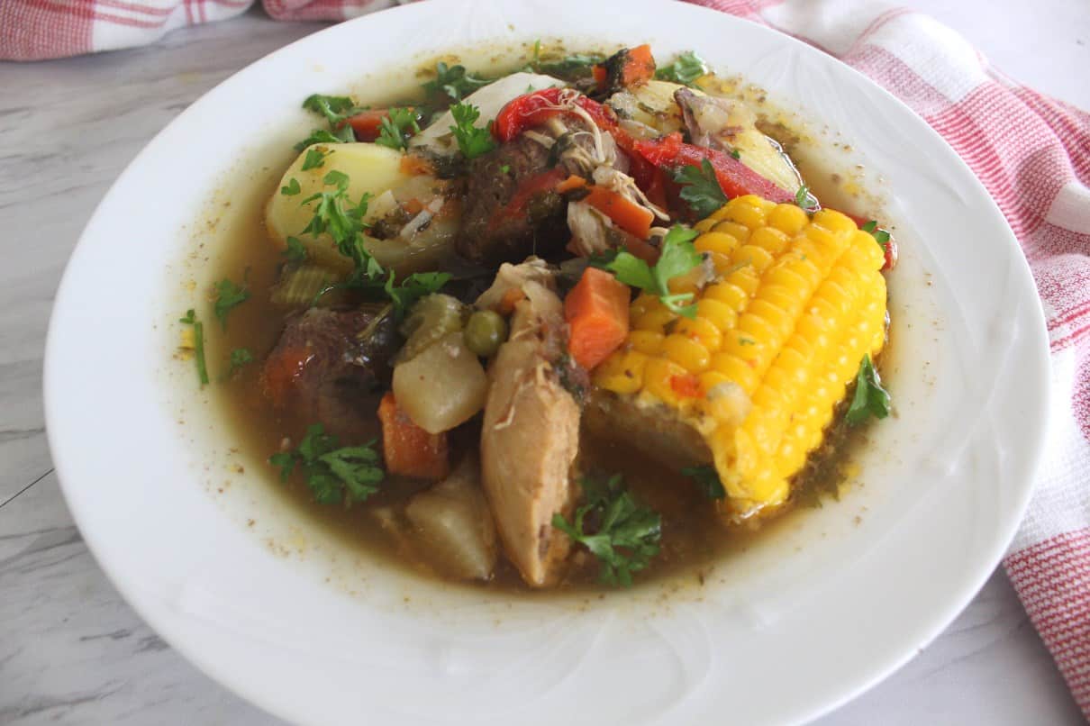A plate of Bolivian Picana (Christmas Soup) - plate shows corn, chicken, beef, vegetables and is decorated with chopped parsley.