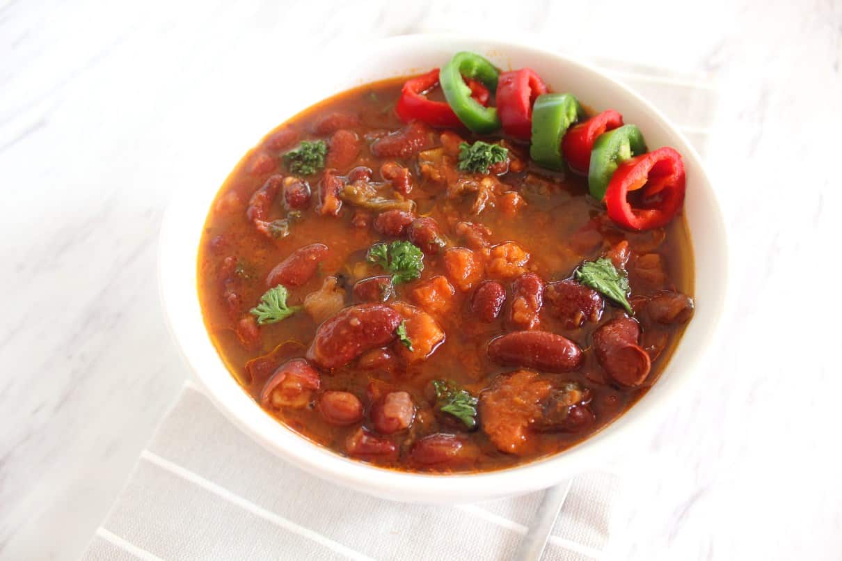 A bowl of red kidney beans soup served with sliced jalapenos and red chilis.