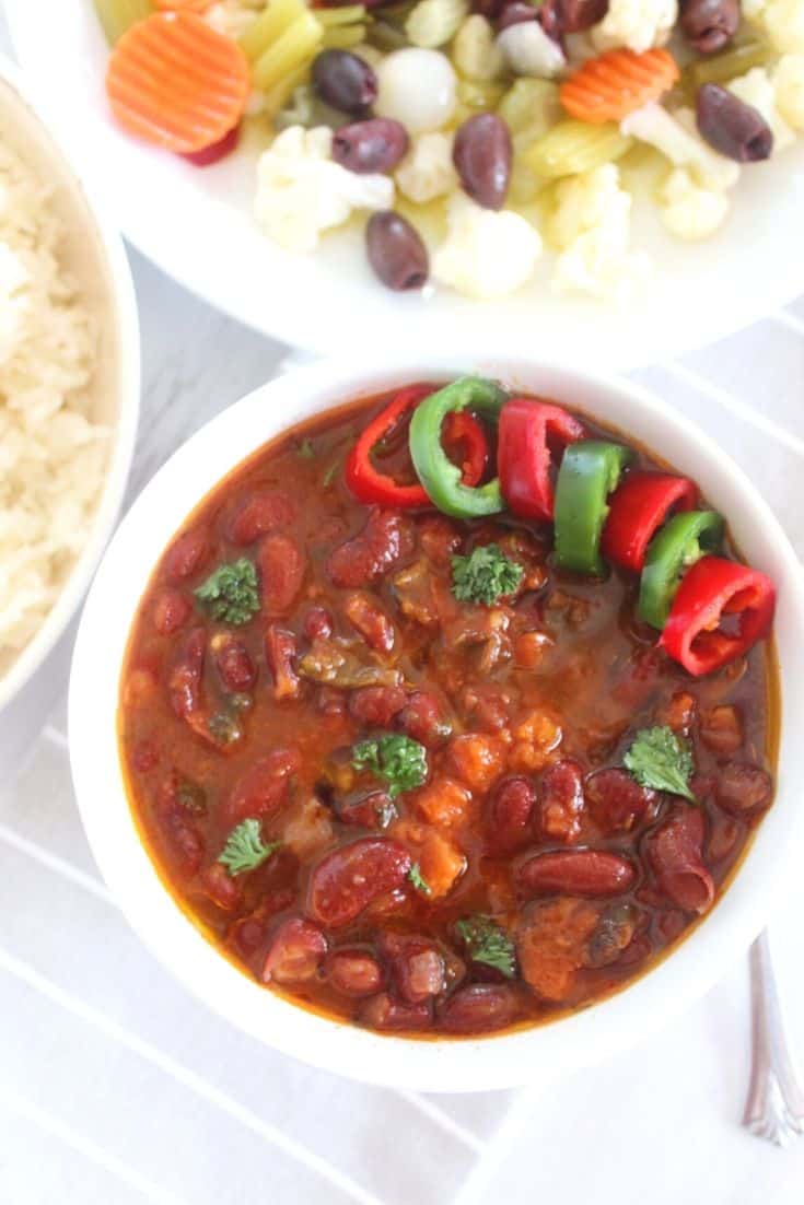 A bowl of red kidney beans soup shown as the focus of the picture, while on the sides you can see rice and a salad with pickled vegetables.