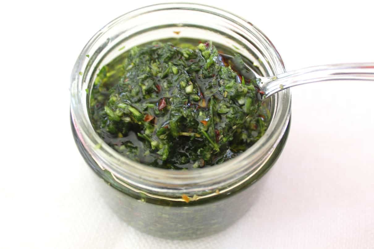 A jar of chimichurri sauce with a spoon ready to serve. 