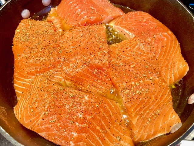 Seasoned salmon fillets cooking in a skillet with extra virgin olive oil. 