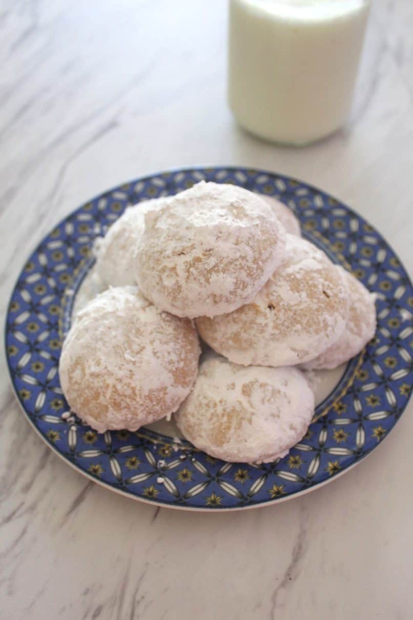 A plate of almond cookies covered in confectioner's sugar next to a glass of milk. 