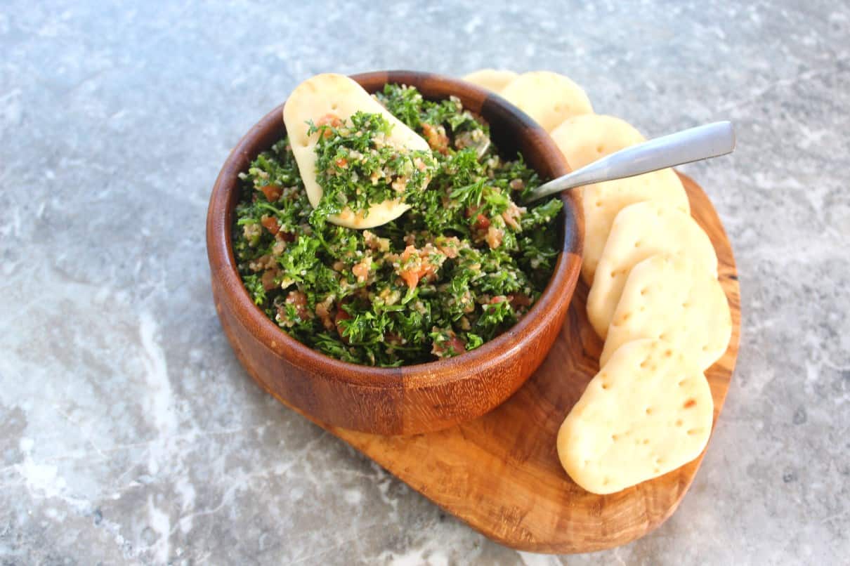 A bowl of tabouli salad served with mini pita breads.