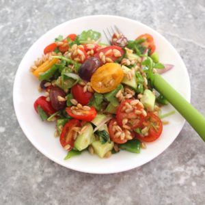 A plate of farro salad with grape size medley tomatoes, cucumbers, green peppers, red onions and kalamata olives.