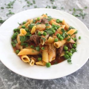 A plate with pasta, meat, green peas and parsley in a red sauce. This dish is called Aji De Fideos in Bolivia.