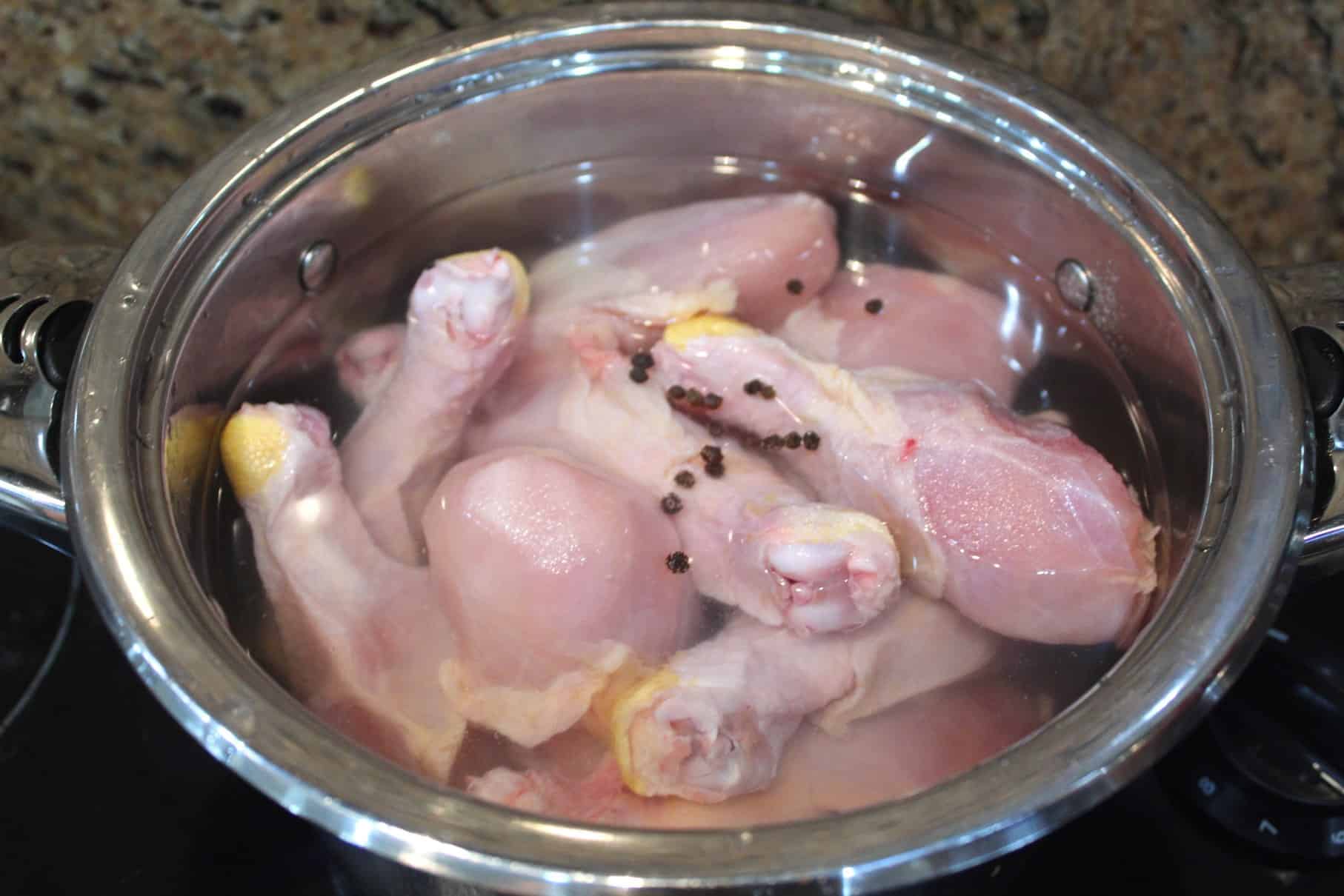 A pot with raw drumsticks shown with some peppercorn and water, ready to cook.