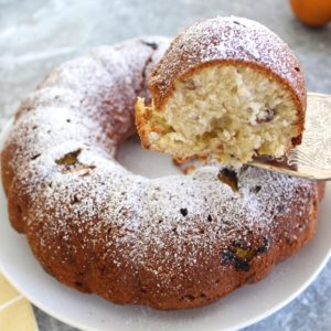 Bundt cake sprinkled with powdered sugar. A cake slice is shown being lifted from the plate.