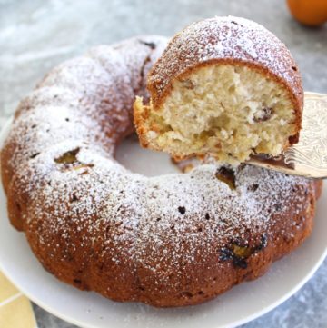 Bundt cake sprinkled with powdered sugar. A cake slice is shown being lifted from the plate.