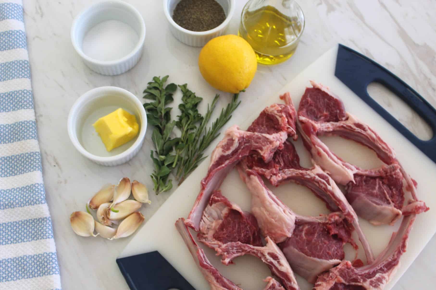 All the ingredients displayed for a visual understanding of what's needed for this recipe. Butter, fresh oregano, fresh rosemary, lemon, olive oil, garlic, lamb chops. 
