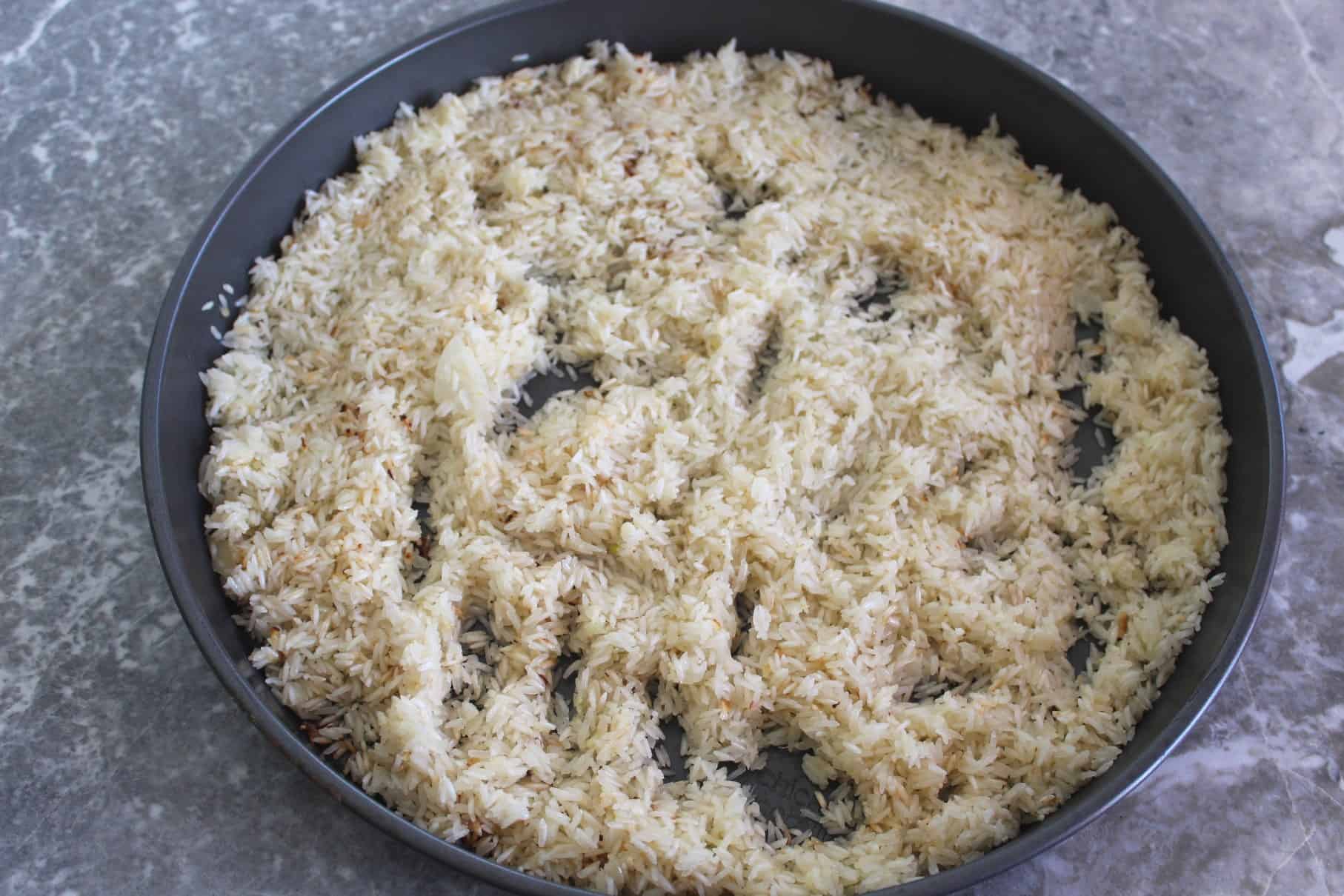 Picture shows a round baking tray with sauteed rice spread in it.