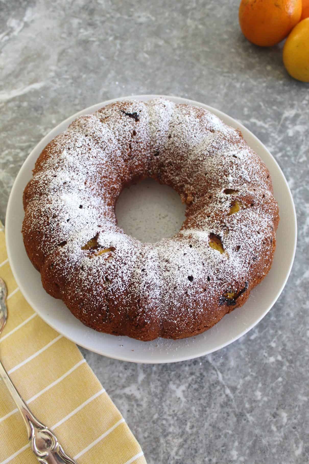 Orange bundt cake with walnuts shown on a white plate, sprinkled with confectioner's sugar.