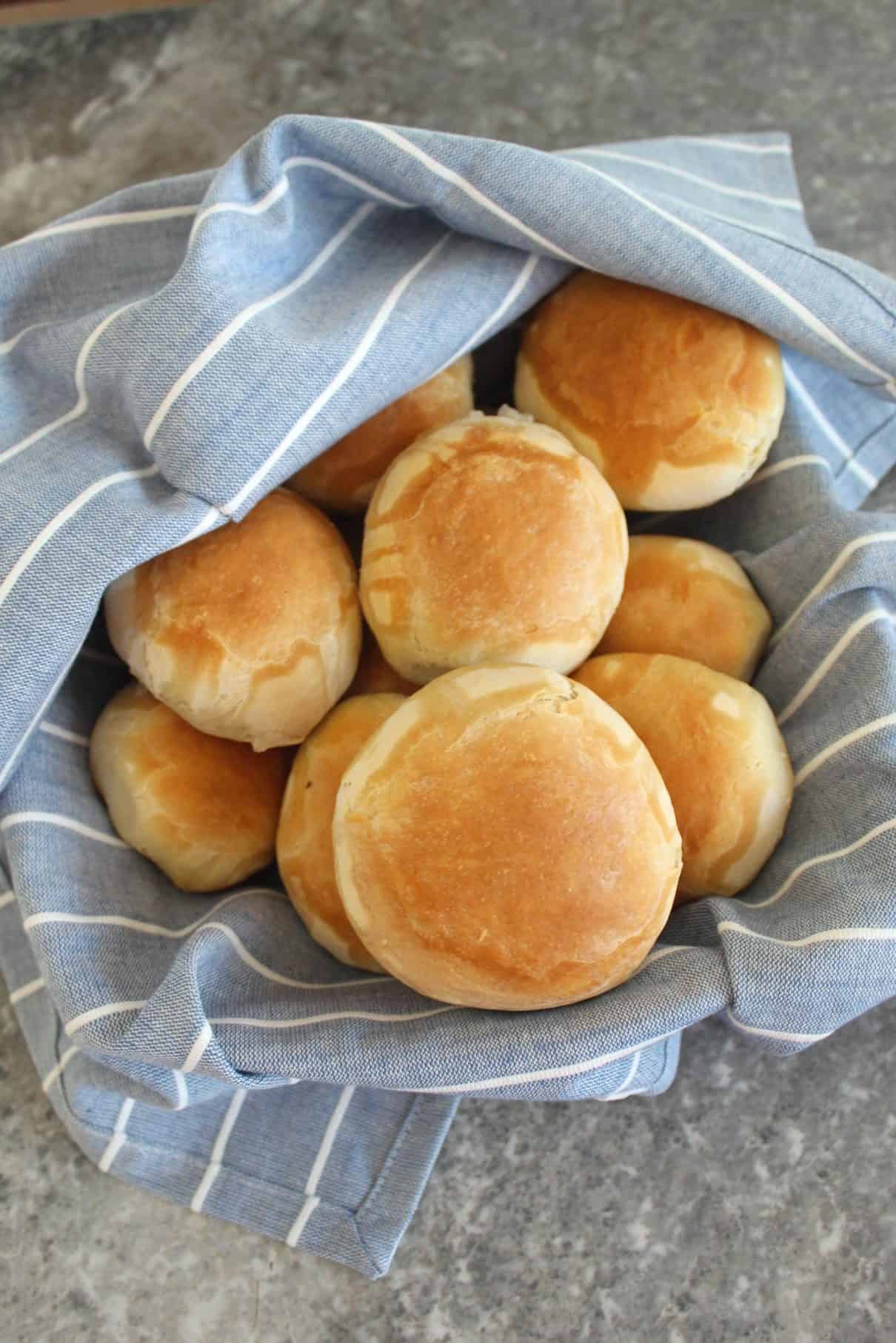 Albanian Home Bread - Bukë shtëpie : picture shows a basket lined with a striped linen. Basket is filled with fresh bread rolls.