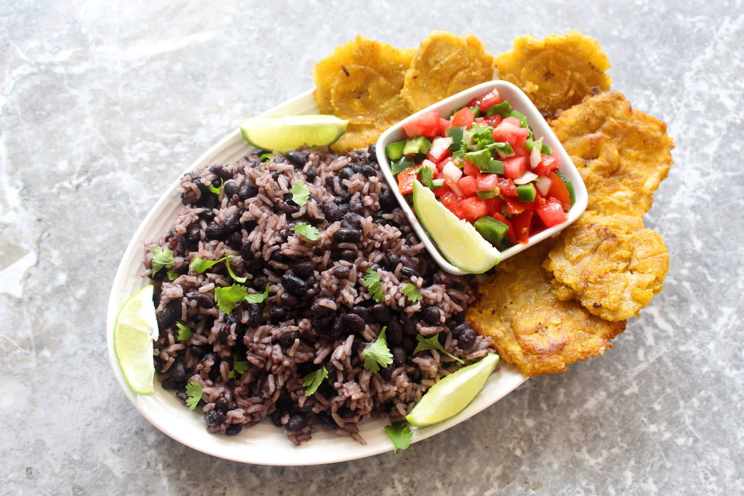 A platter with rice and black beans, pico de gallo, lime wedges and tostones.