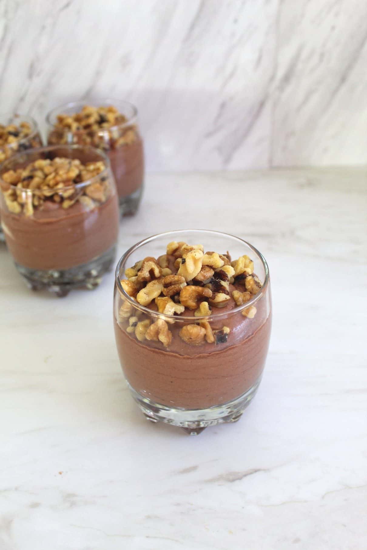 A jar of chocolate mousse topped with walnuts in foreground, and similar jars in the background. 
