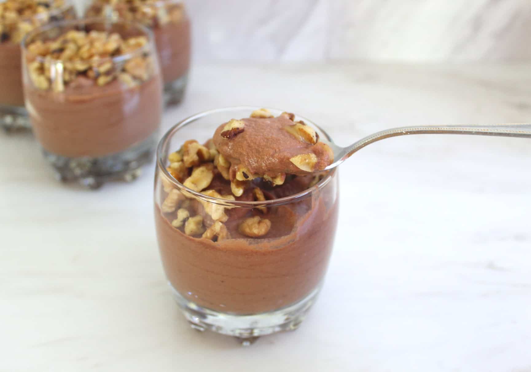 A spoonful of chocolate mousse and chopped nuts coming out of a jar.
