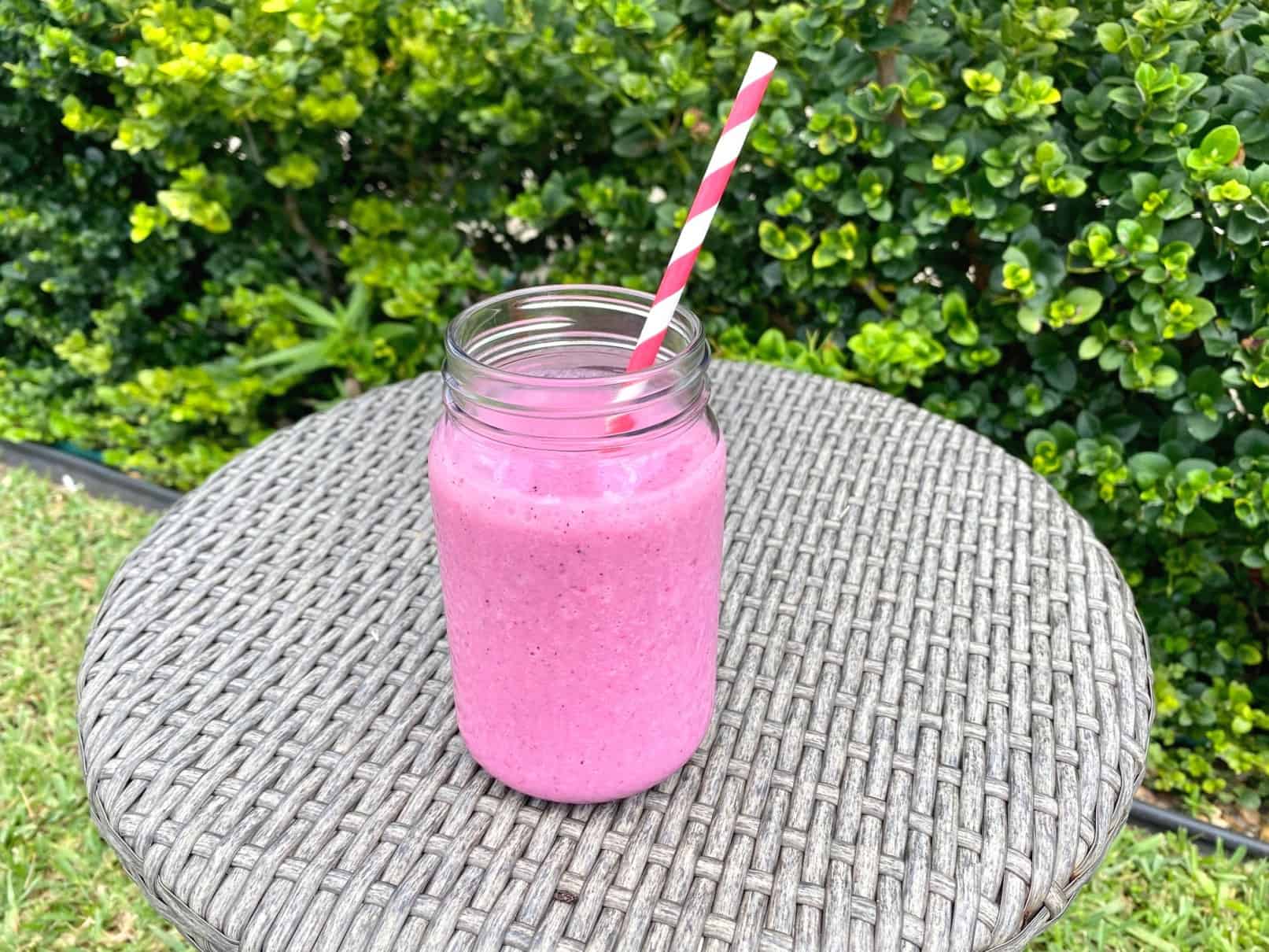 Dragon Fruit Smoothie, shown outdoors on a table facing some green plants.