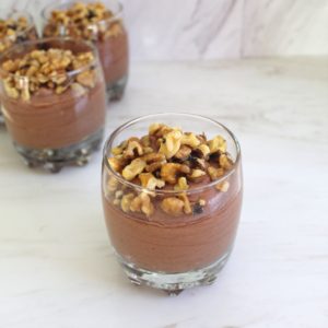 Jars of chocolate mousse topped with walnuts, one jar upfront and the others in the background.