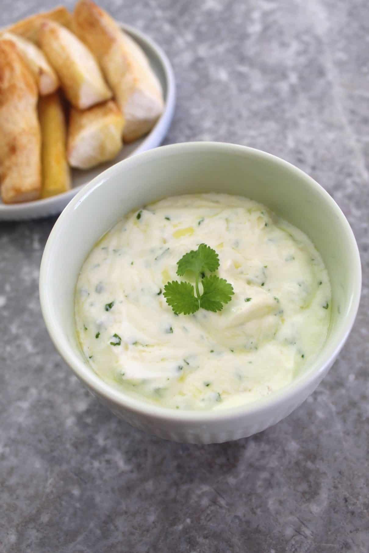 Yogurt based dip with garlic and cilantro, garnished with cilantro and shown next to a plate with fried yucca.
