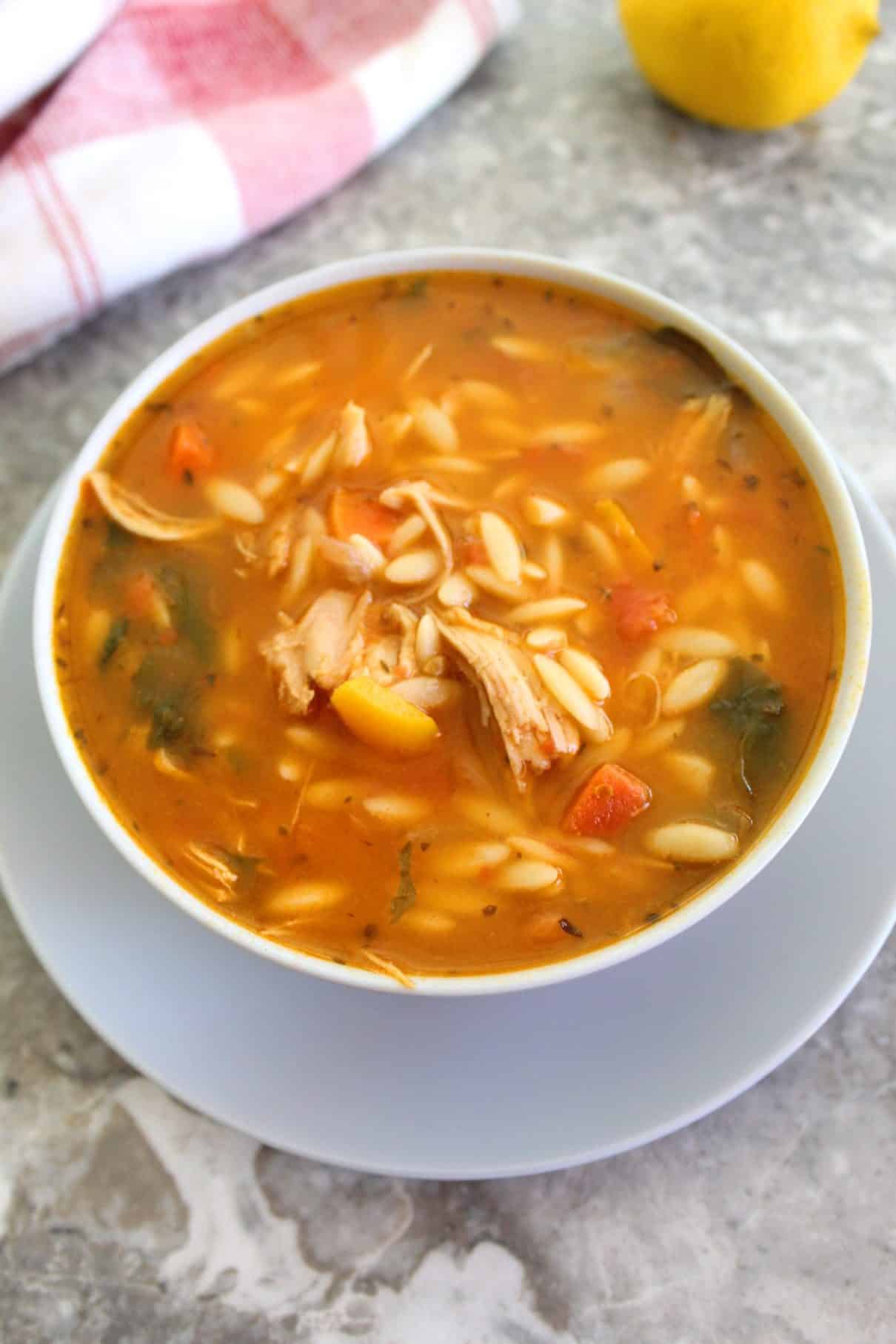 An appetizing bowl of orzo soup showing some shredded turkey, spinach and other vegetables swimming in the soup in a close up shot.