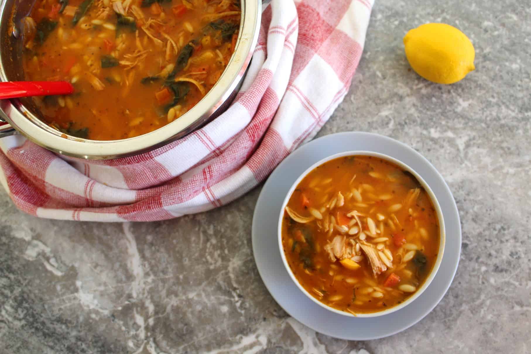Orzo soup with shredded turkey and spinach!! Picture shows a bowl of the soup already served, the pot where it was cooked with a ladle in and a lemon on the other side.