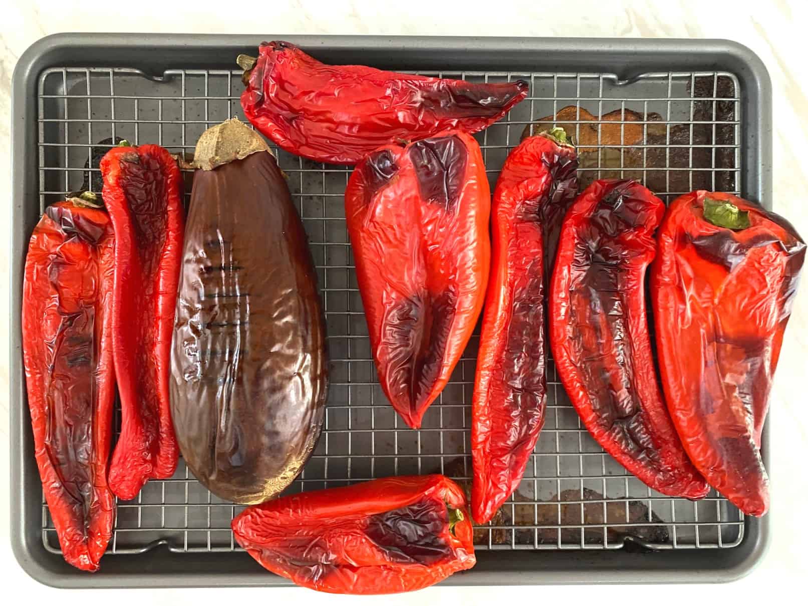 Roasted red peppers and eggplant on a baking tray that has a rack under the vegetables.
