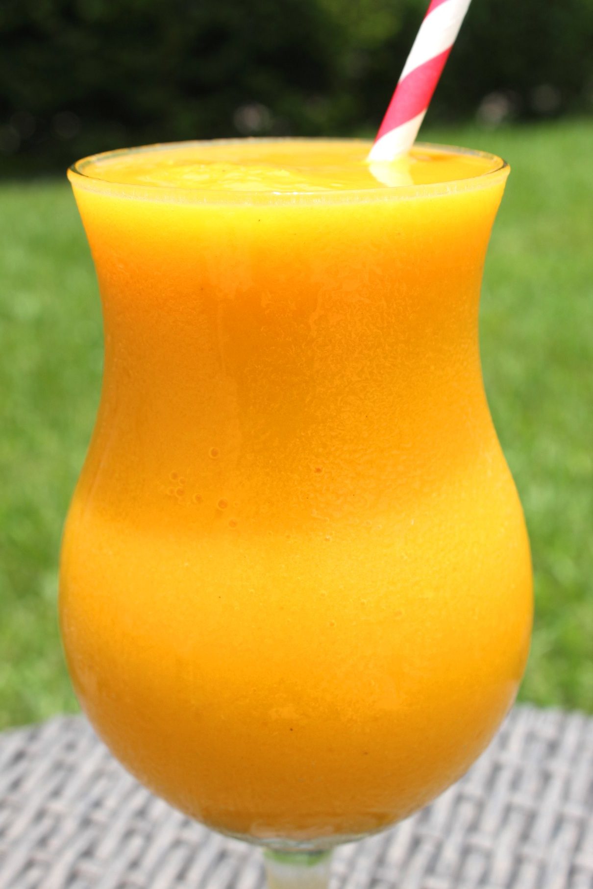 A glass of a yellow/orange frozen cocktail with a paper straw