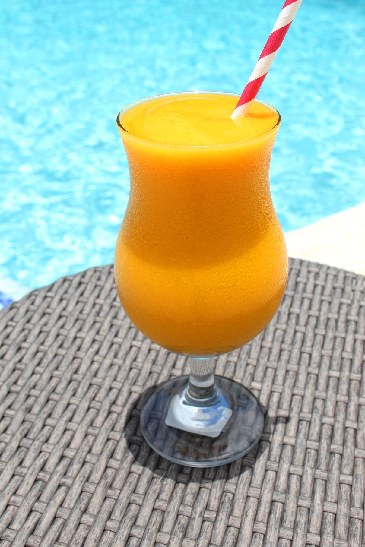 A poolside table with a frozen cocktail on it, ready to be enjoyed. Frozen drink looks tropical.
