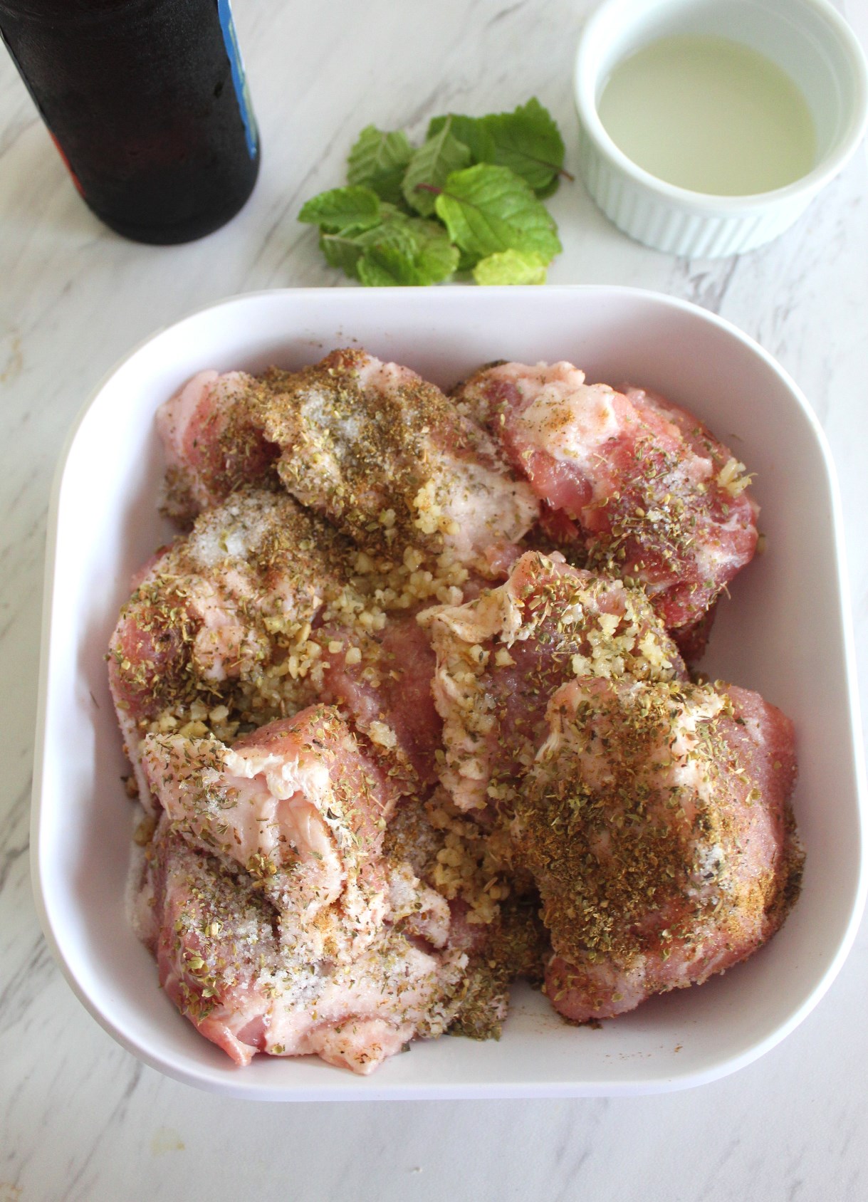 Seasoned pork meat on a wide, square bowl shown next to a beer bottle, mint and lemon juice.