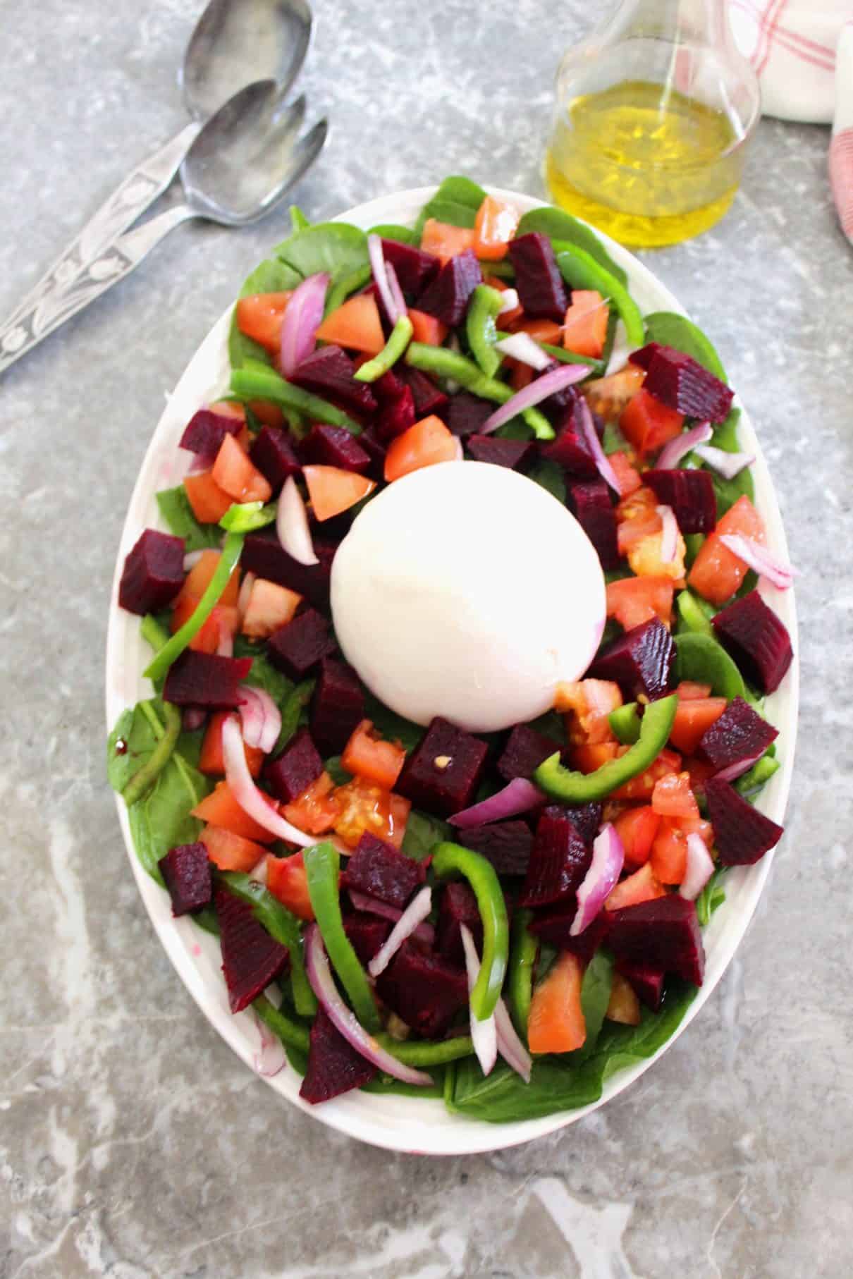 Oval salad platter with lots of colorful vegetables, topped with a burrata. 