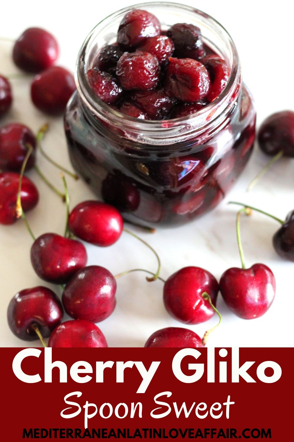 Cherry spoon sweet shown in a jar, surrounded by fresh cherries. Image is prepared specifically for Pinterest because it is shown with a banner that has the title Cherry Gliko across.