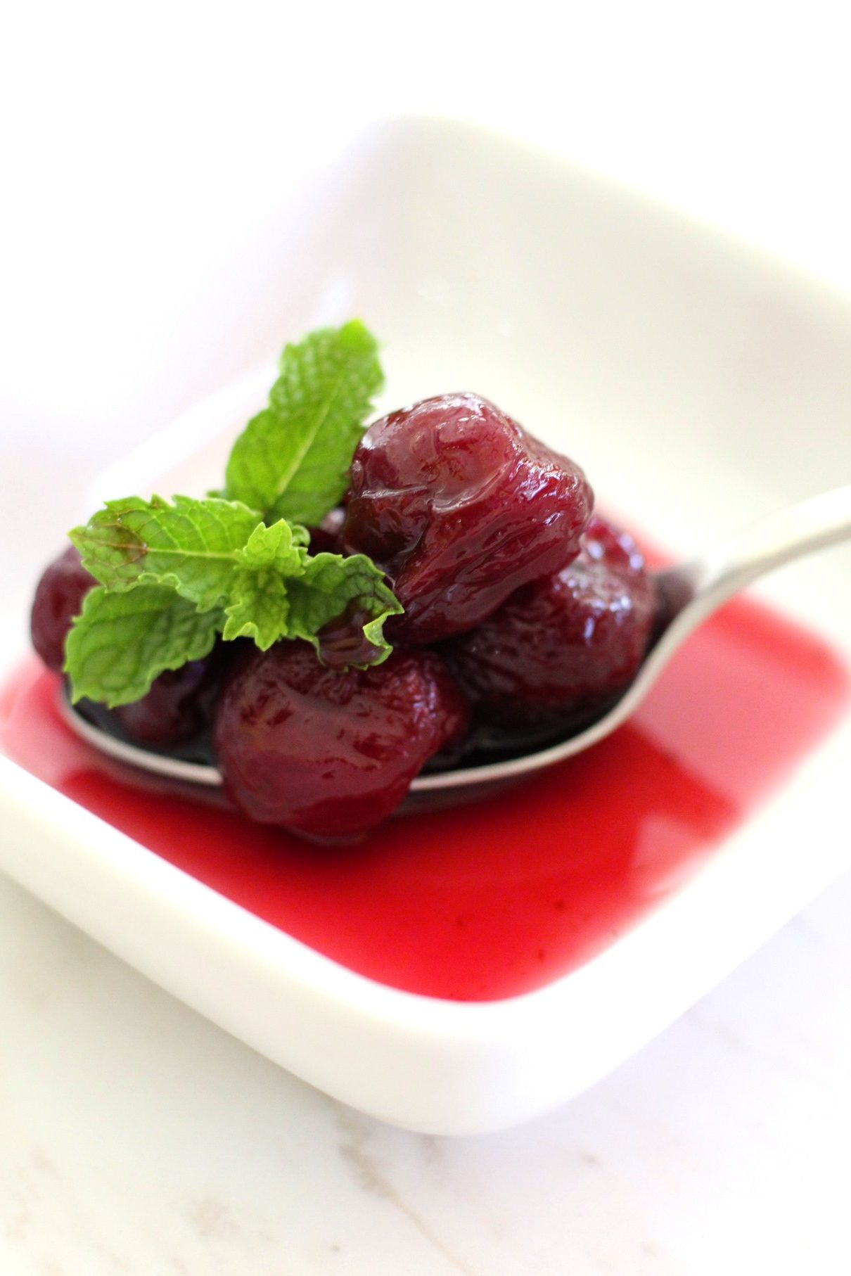 A serving of Cherry Spoon Sweet preserve on a spoon, garnished with mint.