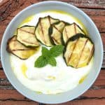 A bowl of yogurt soup with zucchini, olive oil and mint. Bowl is shown on some rustic surface.