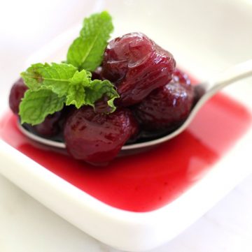 A spoon of Cherry Spoon Sweet garnished with mint on a small plate