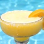 A frozen margarita drink next to a pool. Cup has a salty rim and the outside of the cup shows condensation.