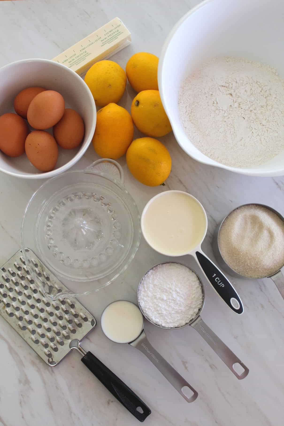 Ingredients in measuring cups and bowls for making Meyer Lemon Bundt cake - eggs, butter, flour, heavy cream, sugar, powder sugar, milk.
