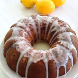 Meyer Lemon bundt cake shown on a round platter with fresh lemons in the background
