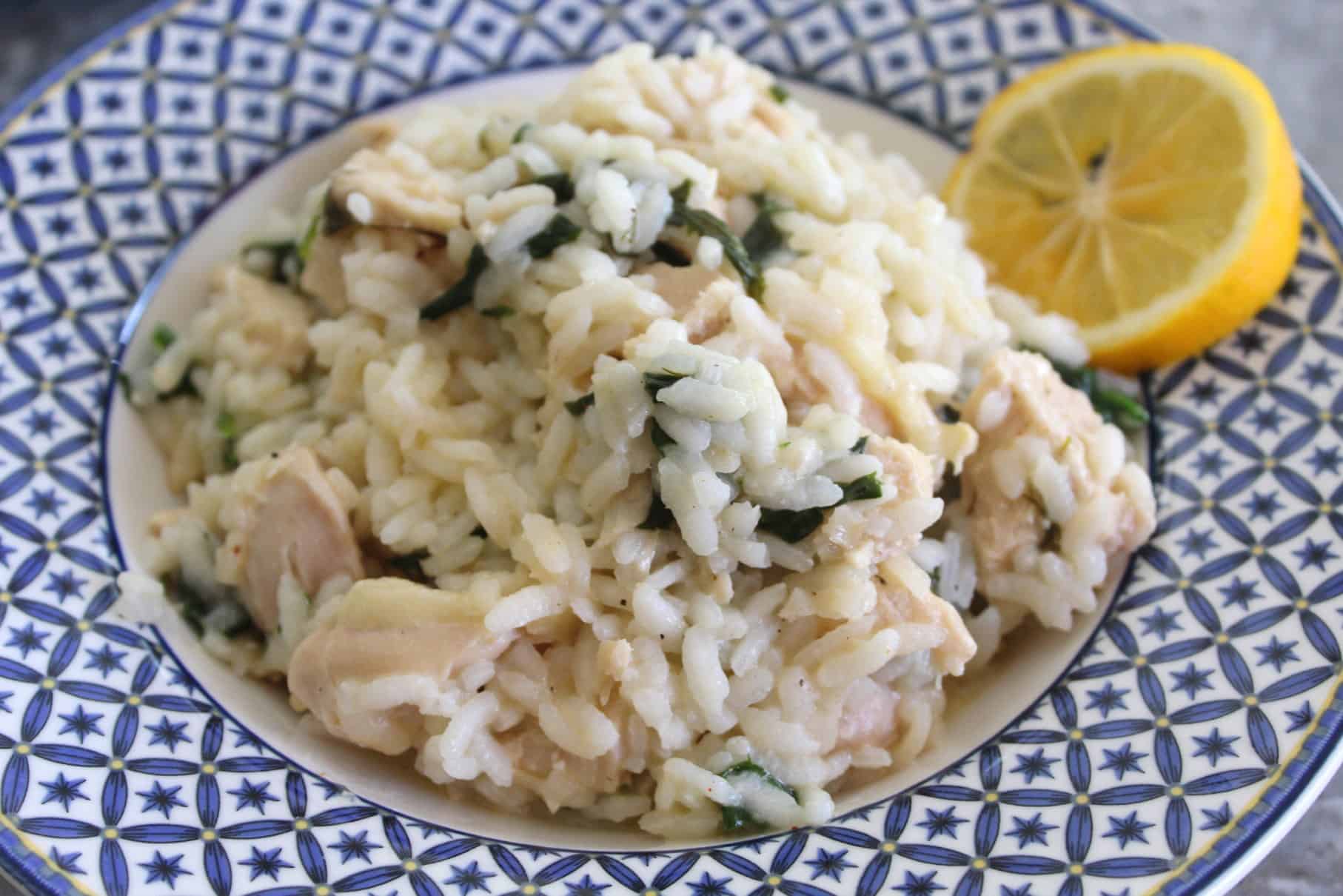 Chicken risotto with lemon, spinach and dill shown in a white/blue round plate and garnished with lemon. 