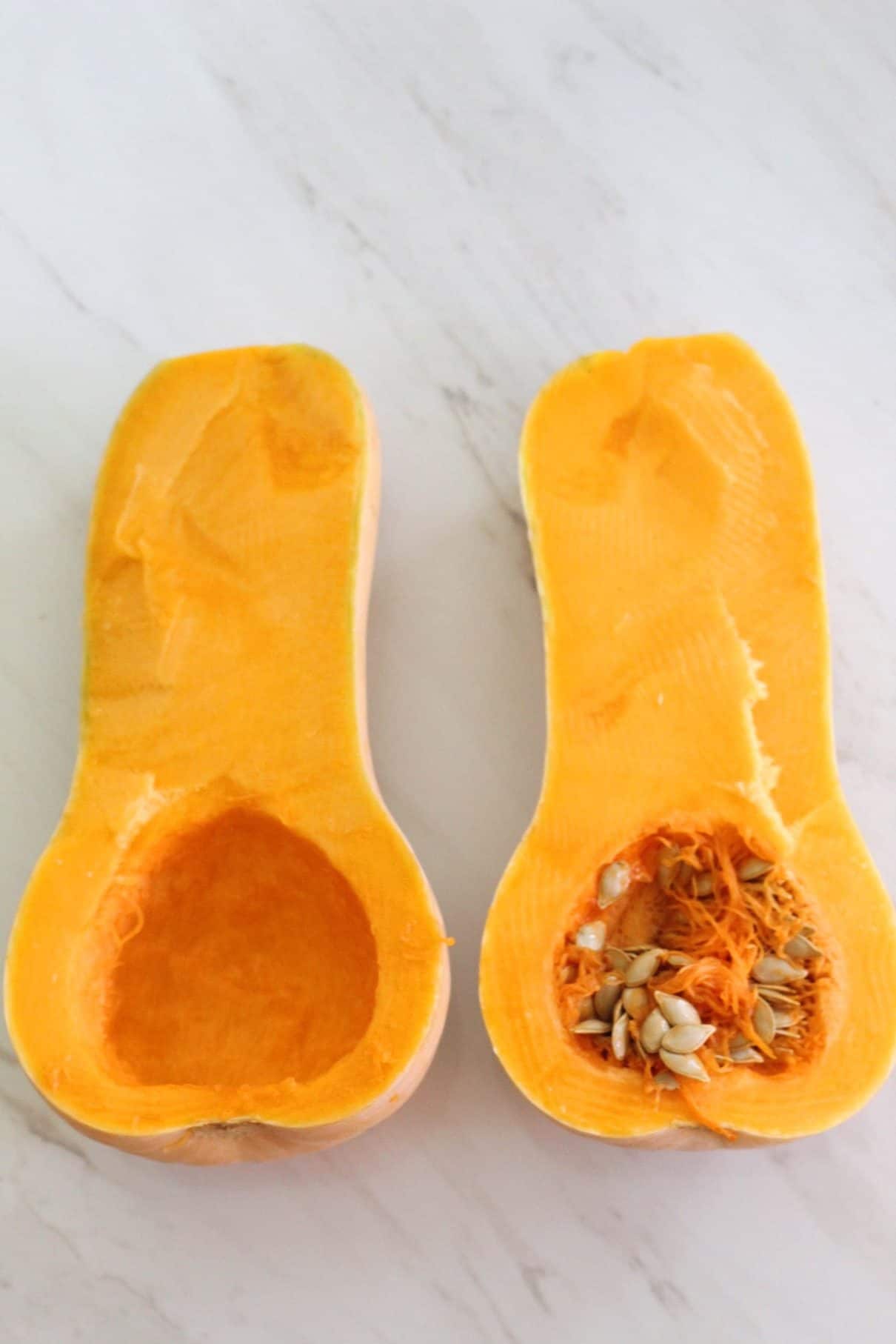 A butternut squash cut in half, one half is already cleaned from seeds and pulp but the other half not.