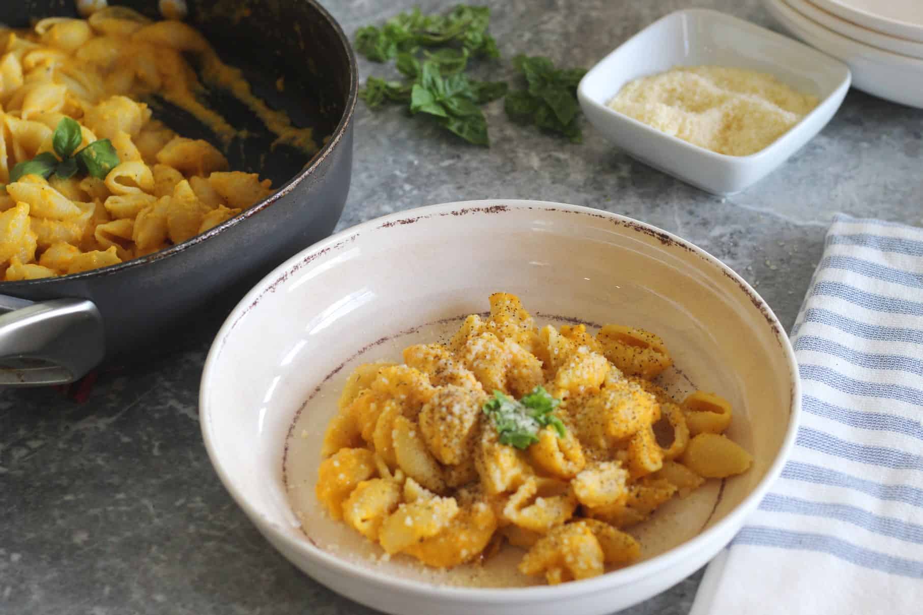A fresh serving of shell pasta with butternut squash sauce. Pasta is served with basil and parmesan cheese, topped with black pepper.