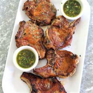 Platter with golden brown, juicy pork chops served with 2 sides of mint chimichurri sauces.
