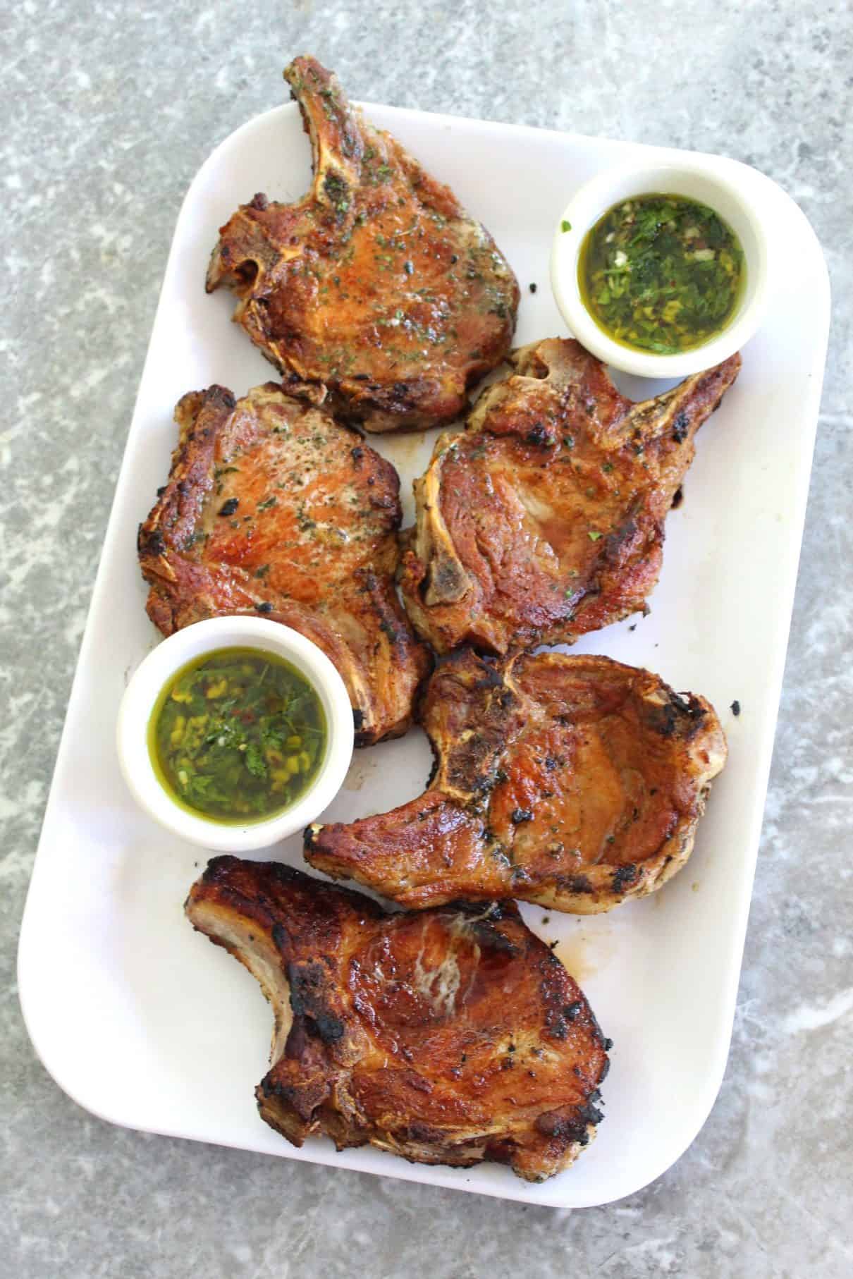 A platter with 5 golden brown, juicy pork chops served with an oily herbed sauce (mint chimichurri).