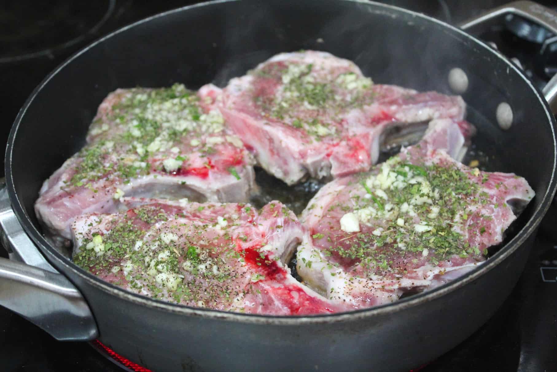 A skillet in high heat over the stovetop, with steaming pork chops inside. 