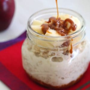 Adding dulce de leche over chopped apples on an oats jar for breakfast!! Jar is placed over a colorful napkin and there's an apple in the background out of focus.