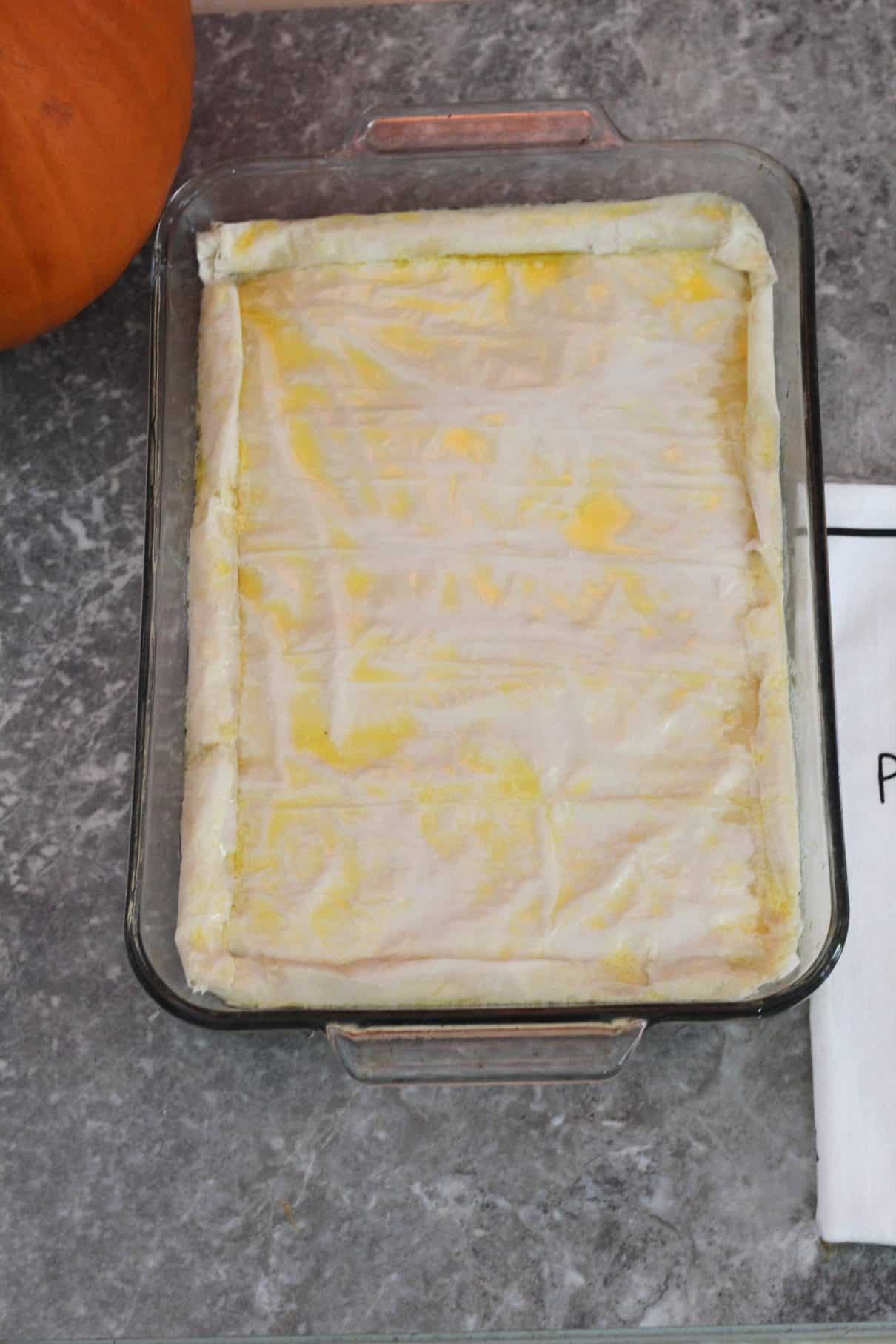 A rectangular baking dish ready to bake with phyllo pie (byrek) brushed with butter. 