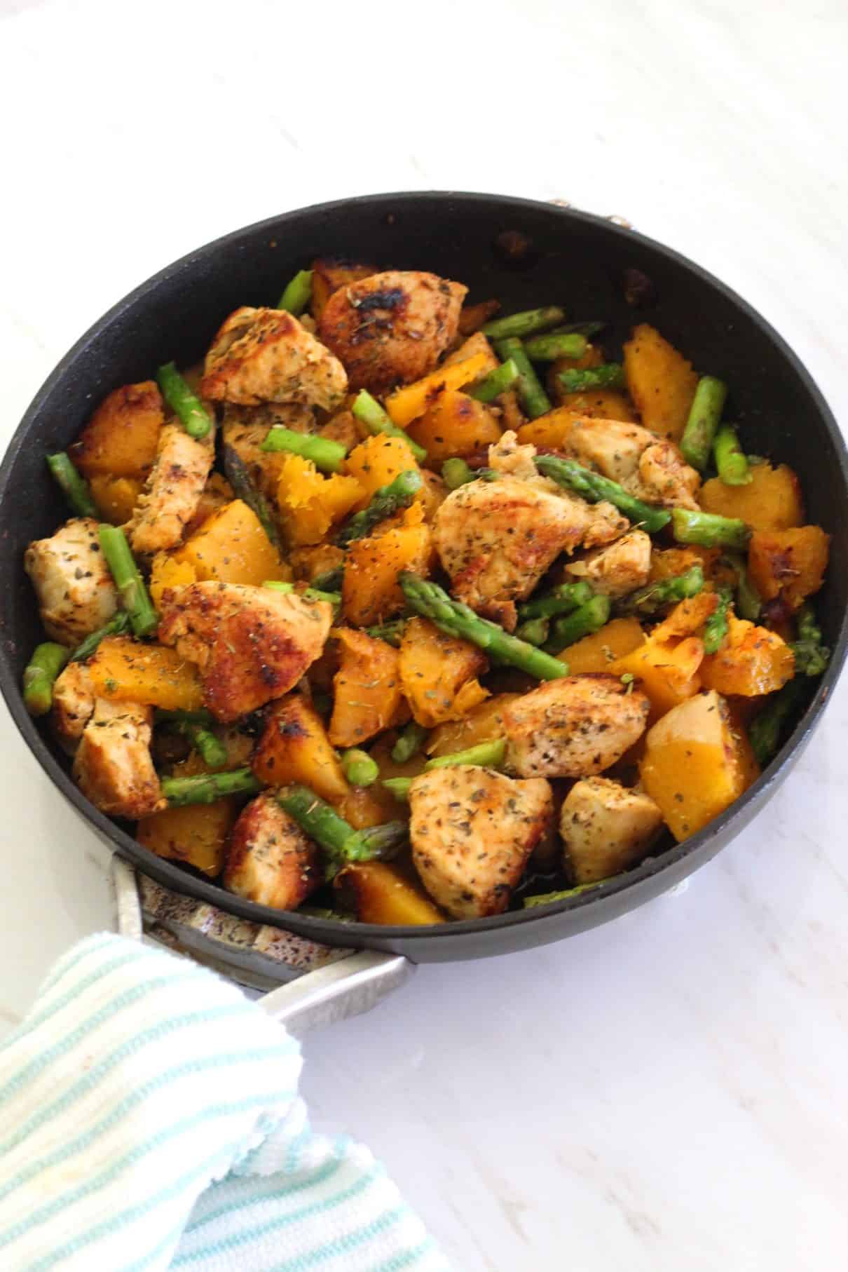 A skillet with cooked dinner: chicken, butternut squash and asparagus.